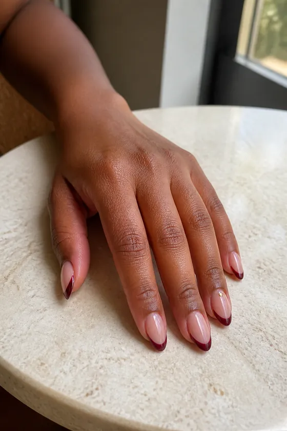 Burgundy French tip fall almond nails on a stone table