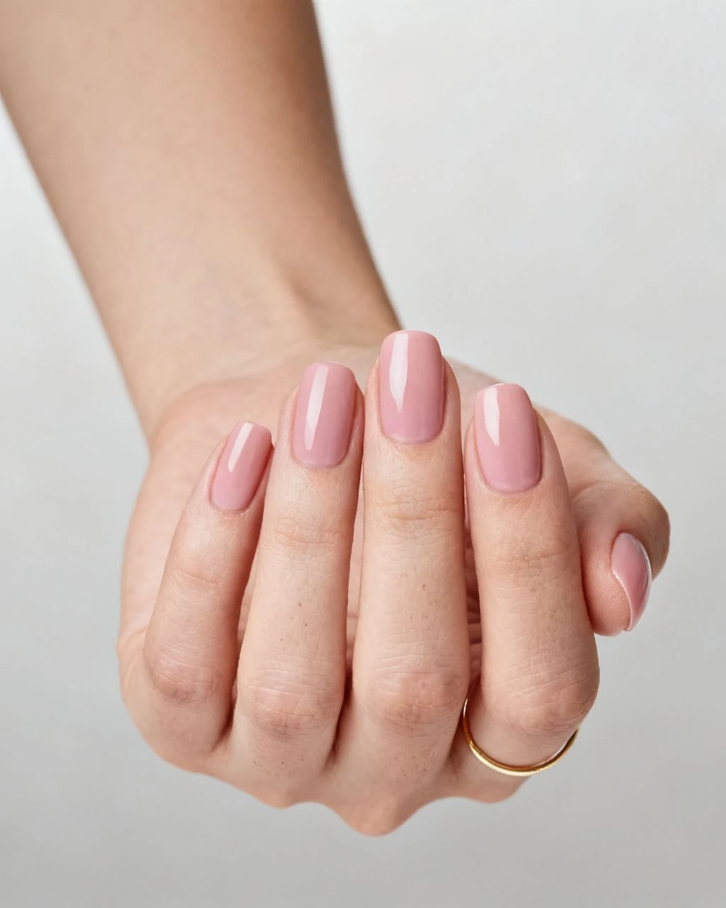 Simple elegant pale blush pink oval manicure on a curled hand against a plain neutral background.