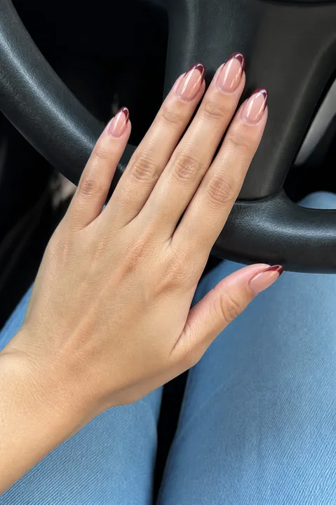 Long almond nails with burgundy French tips in a car