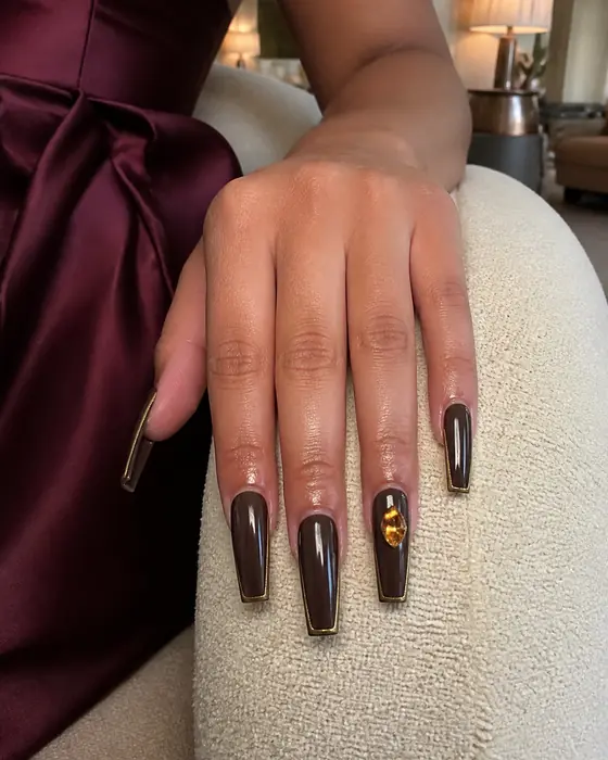 Long espresso coffin fall nails with gold outline on a chair arm