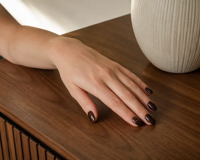 Deep espresso oval acrylic nails on a walnut table