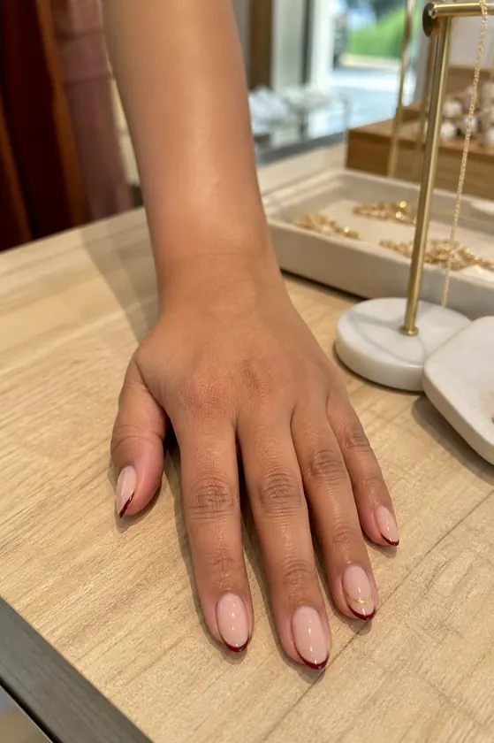 Burgundy and gold micro French fall nails on a boutique counter
