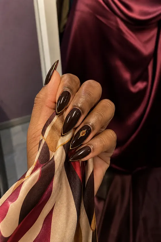 Espresso brown and gold outline fall stiletto nails holding a silk scarf