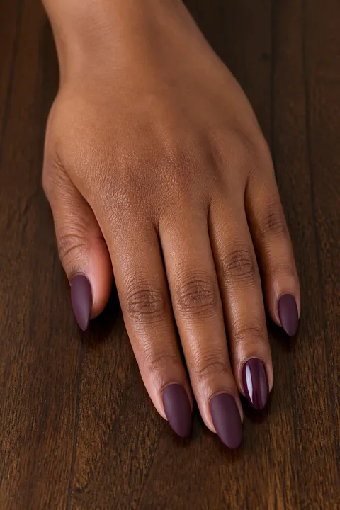 Matte plum almond nails resting on a dark wooden table