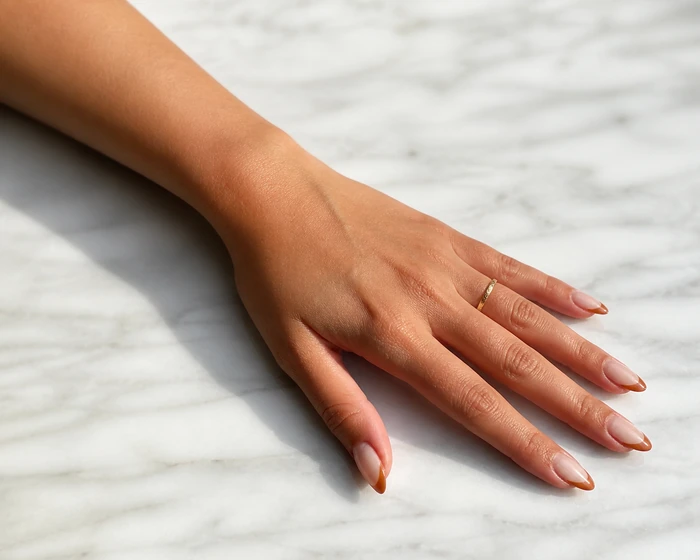 Caramel French tip gel nails on a pale marble table