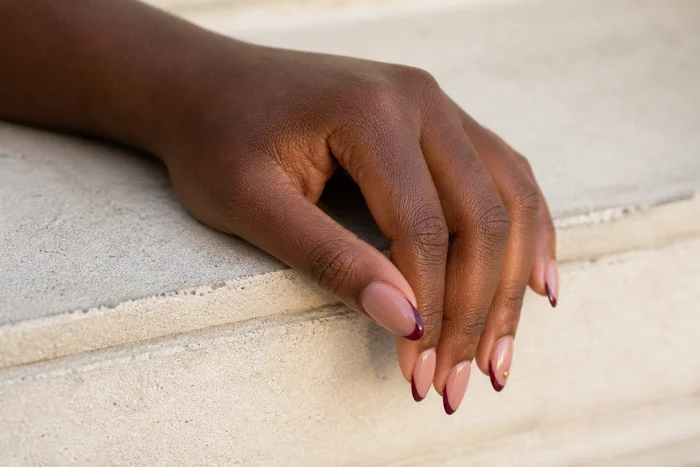 Burgundy micro French acrylic nails resting on a stone bench