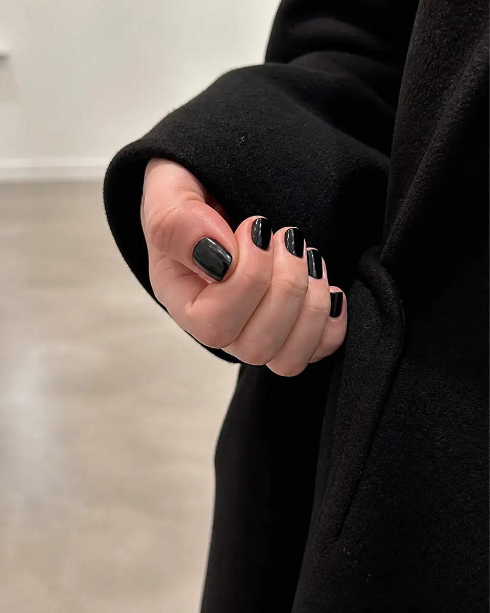 Simple glossy black squoval nails with a black wool coat.