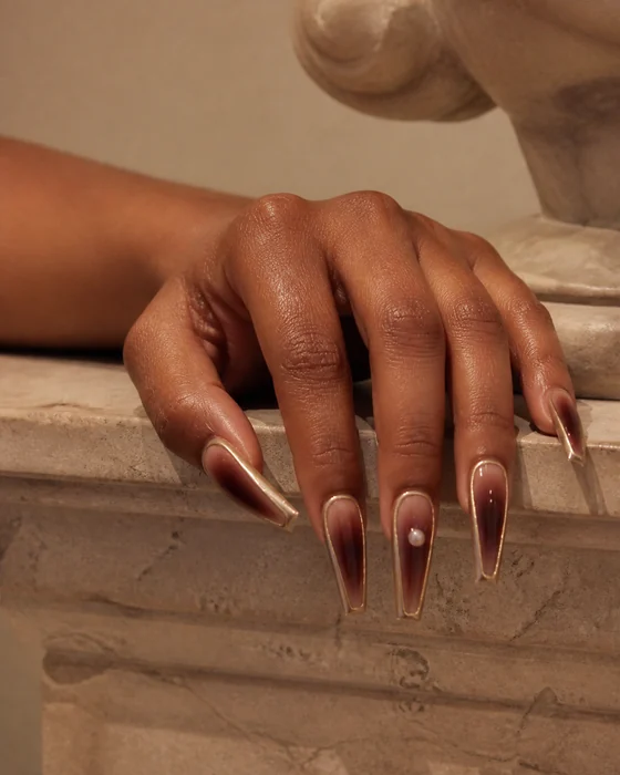 Long burgundy aura coffin fall nails with copper chrome on a stone plinth