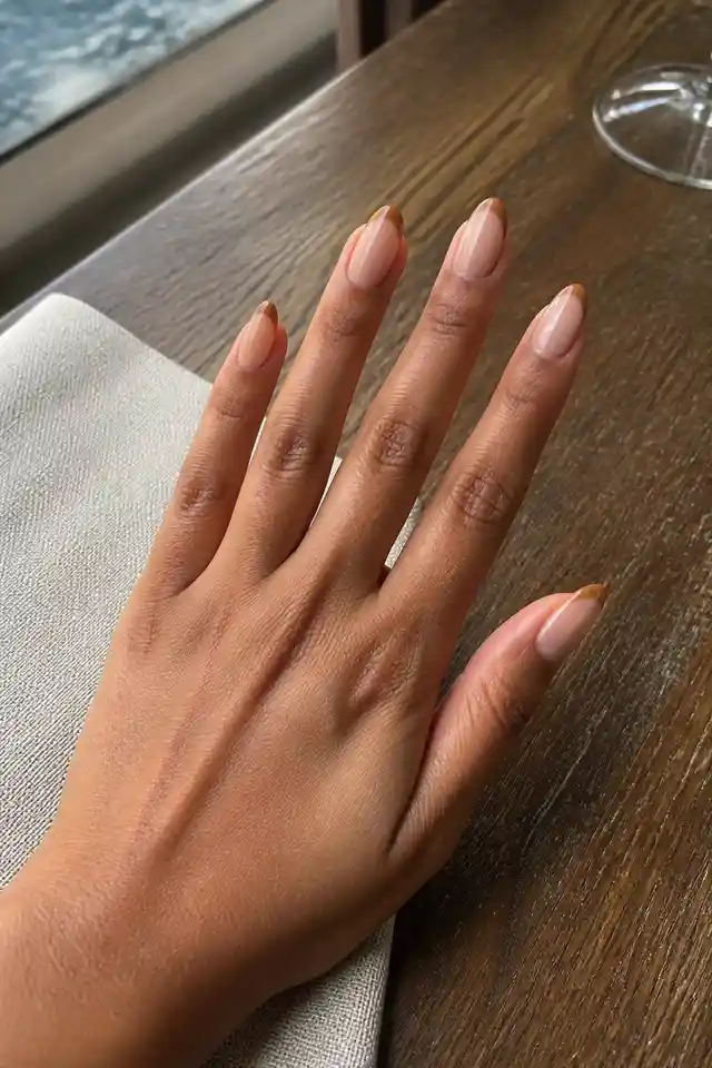 Caramel almond French tip fall nails on a woman’s hand holding a latte.