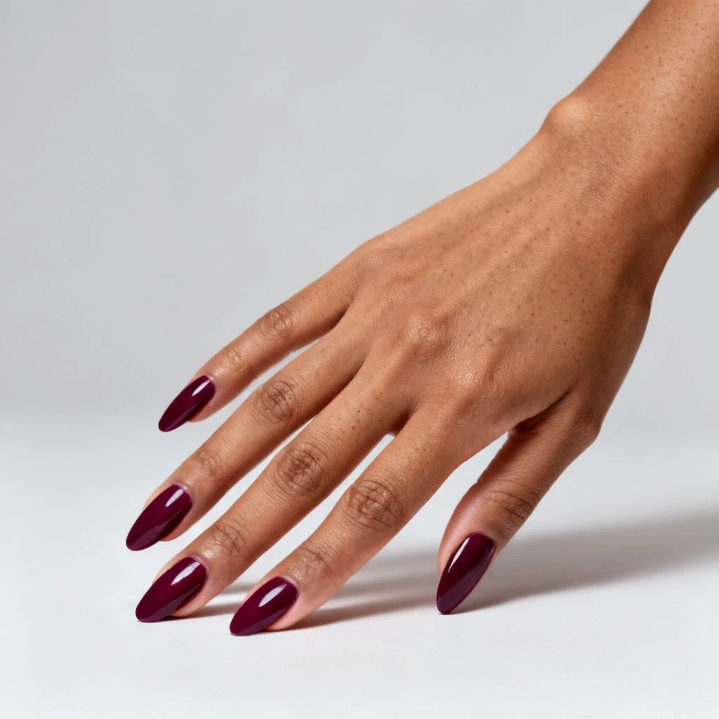 Rich deep plum almond nails on a single hand against a plain neutral studio background.