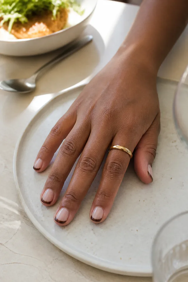 Short natural nails with slim brown French tips.