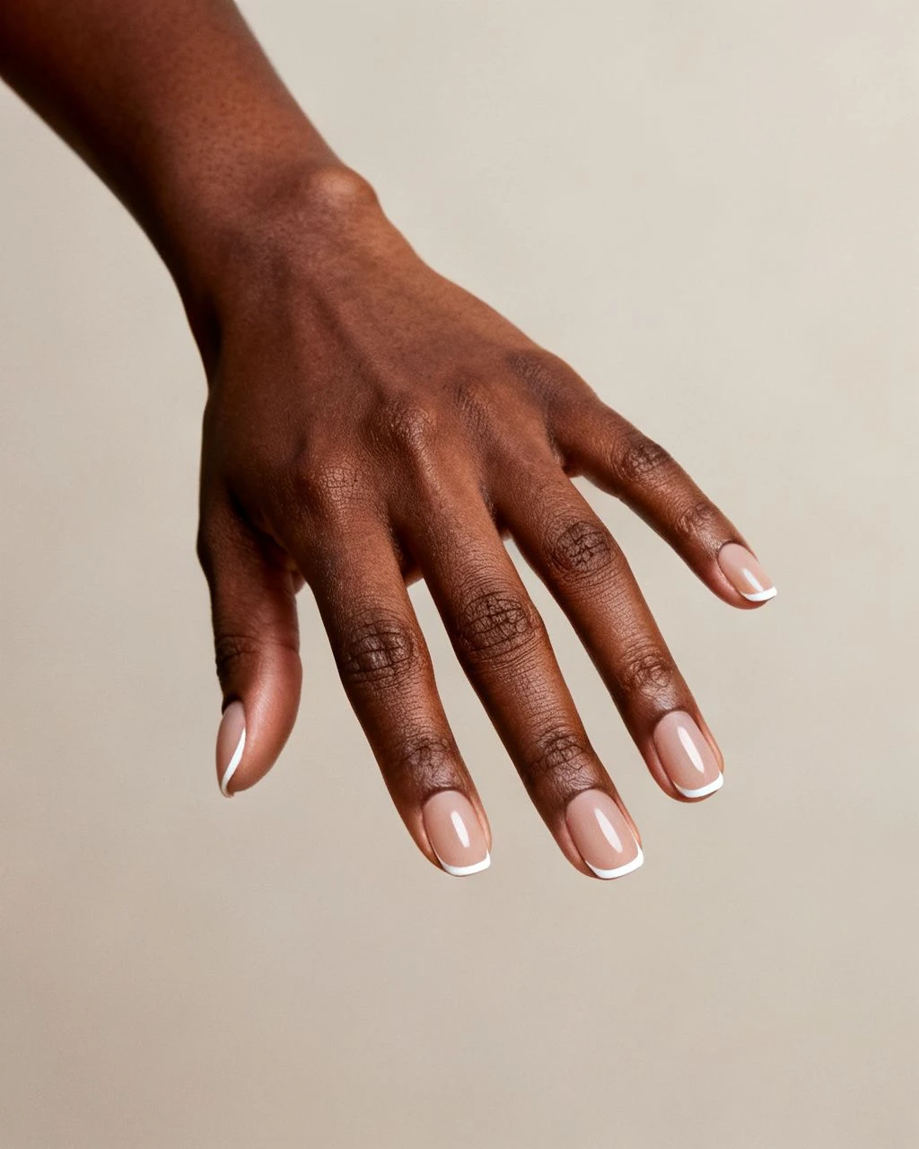 Thin white French tip almond nails on a Black woman's hand against a plain neutral studio background.