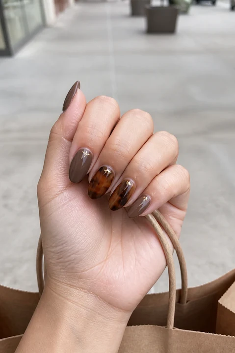 Mocha tortoiseshell nails with subtle gold detail while holding a paper shopping bag