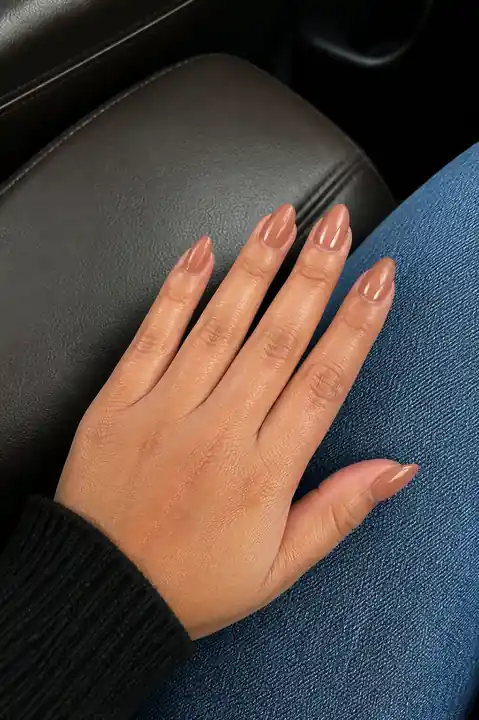 Warm nude glazed almond nails on denim in a car