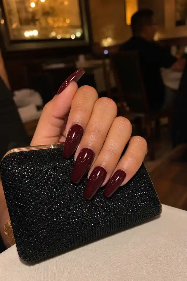 Burgundy coffin fall nails on a woman’s hand against a dark autumn outfit.