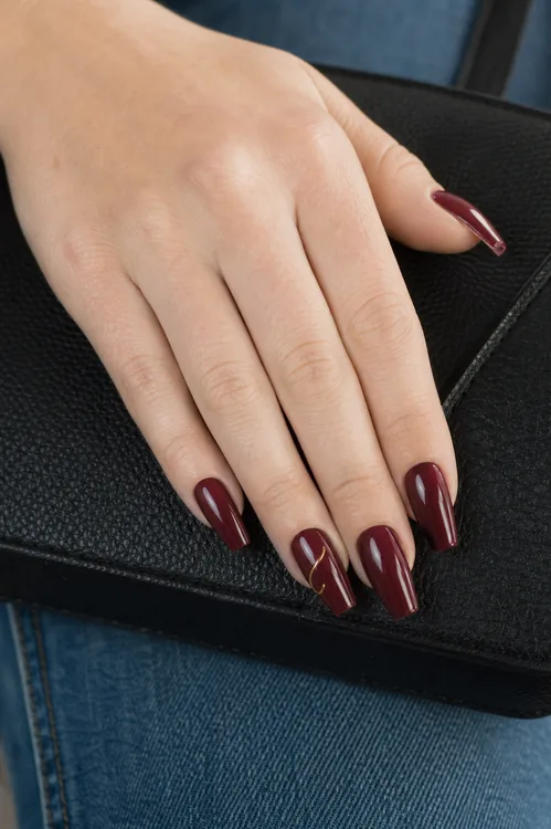 Burgundy coffin nails with gold line art resting on a handbag