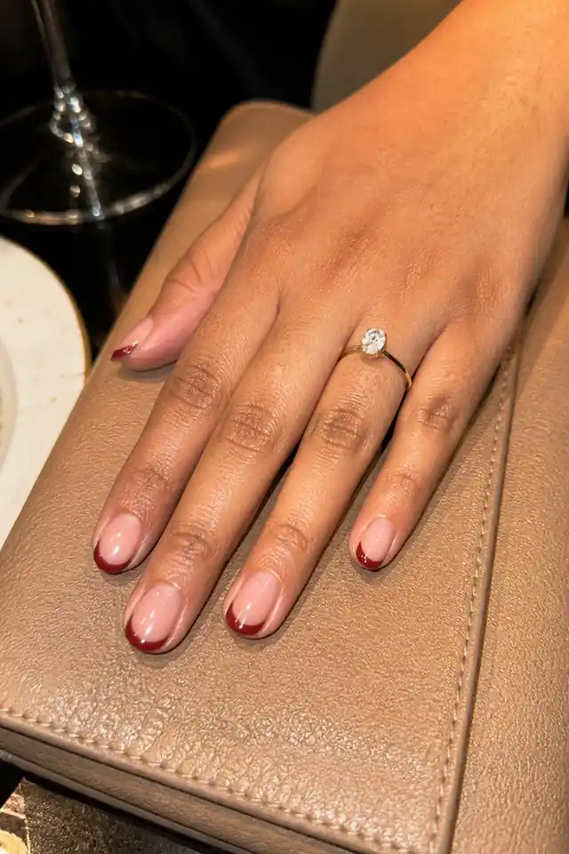 Short natural nails with slim burgundy French tips.