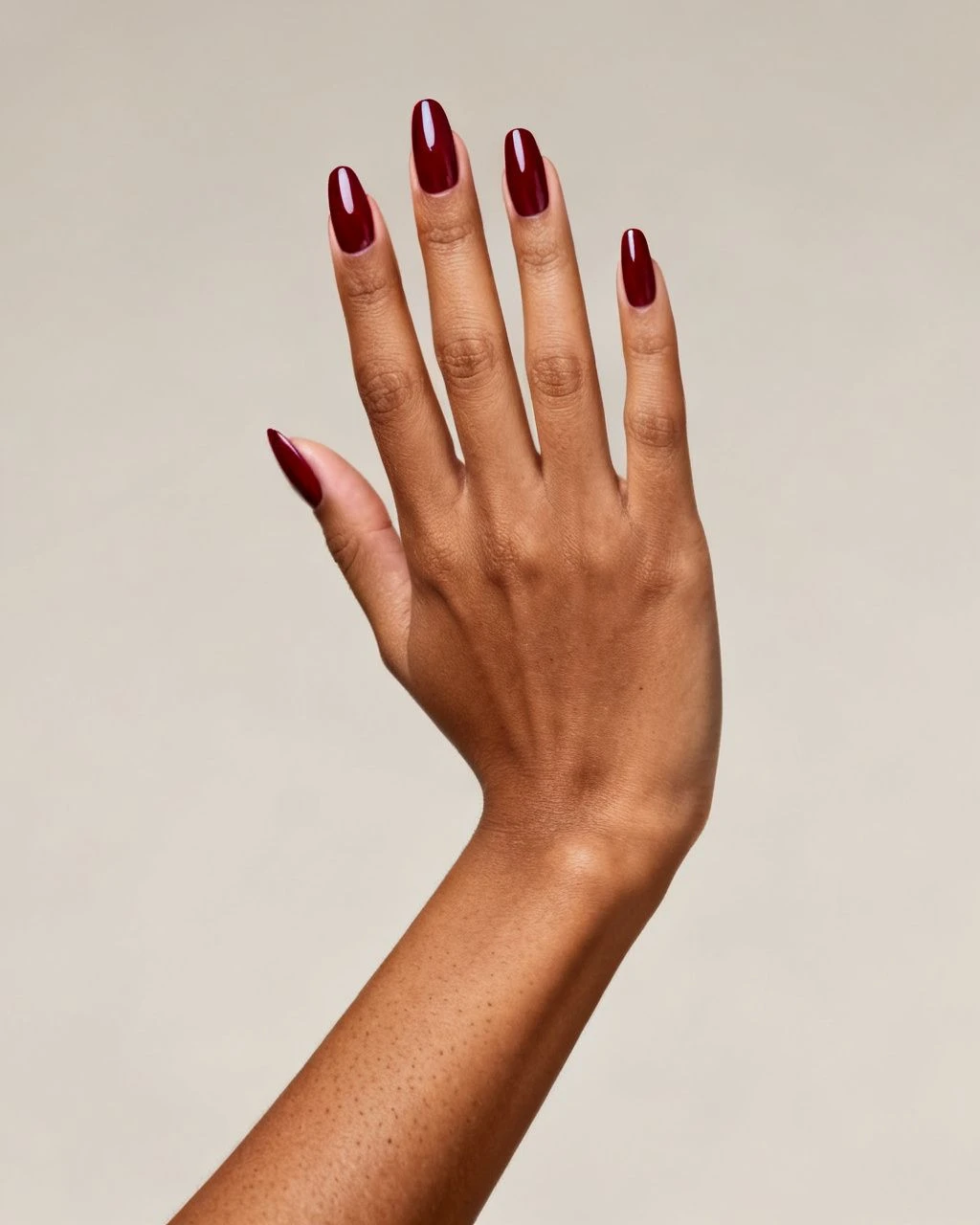 Deep berry-red almond nails on a hand against a plain neutral studio background.