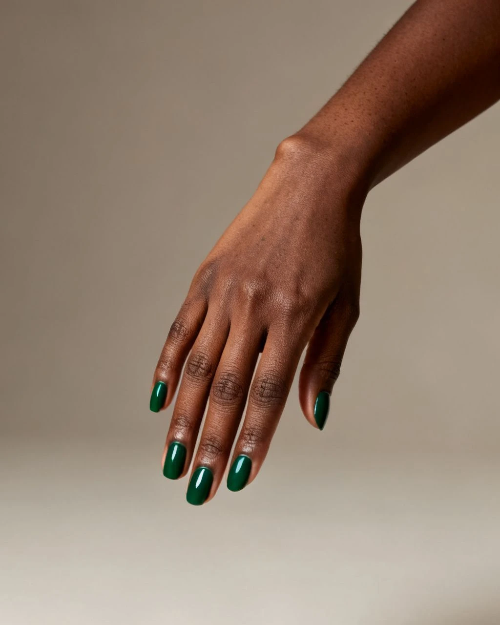 Deep emerald-green oval nails on a Black woman's hand against a plain neutral studio background.