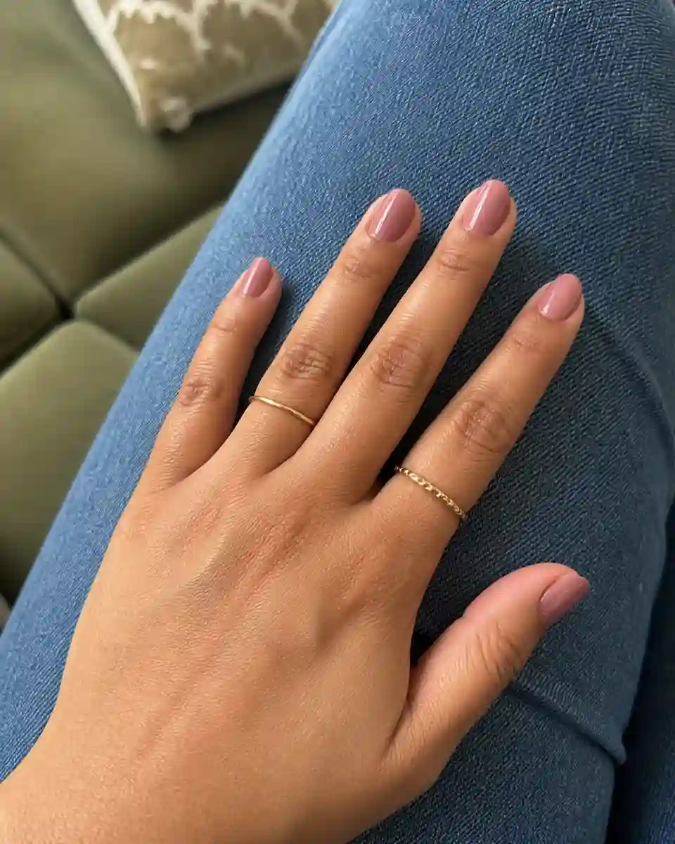 Short soft mauve-pink elegant nails resting on blue denim.