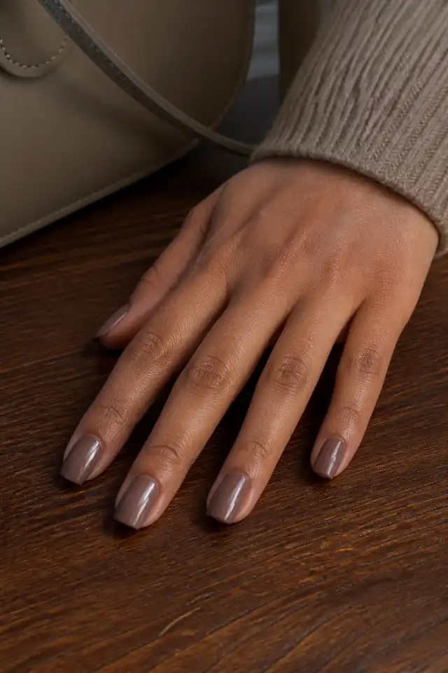 Mocha chrome fall nails on a woman’s hand holding a leather clutch.