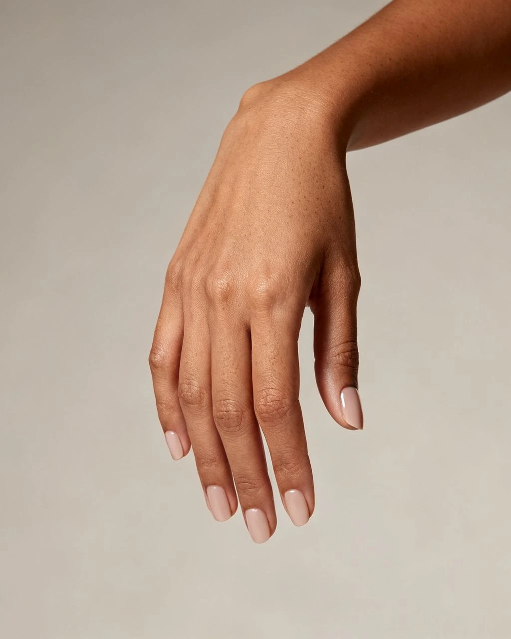 Short clean sheer nude nails on a hand against a plain neutral studio background.