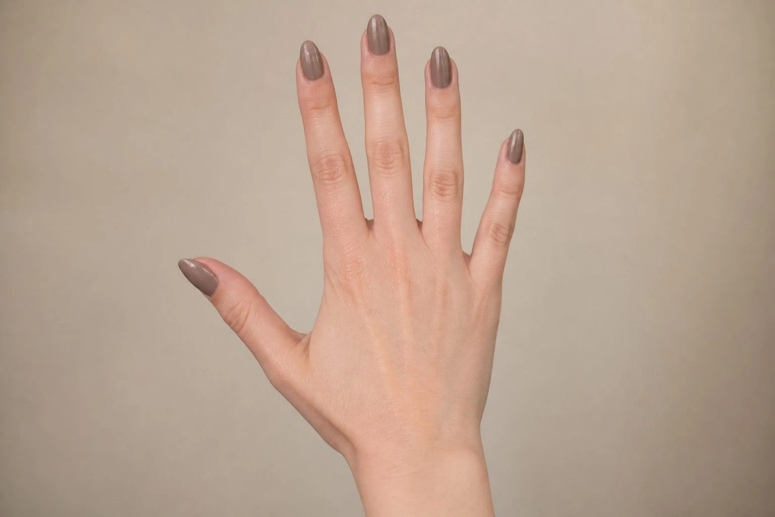 Warm taupe almond nails on a hand with fingers spread, hand-only studio macro shot