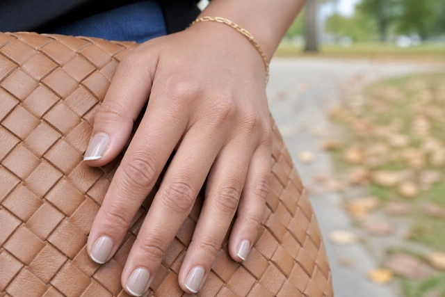Warm Greige Micro French autumn nails on a woman’s full hand in a natural setting.
