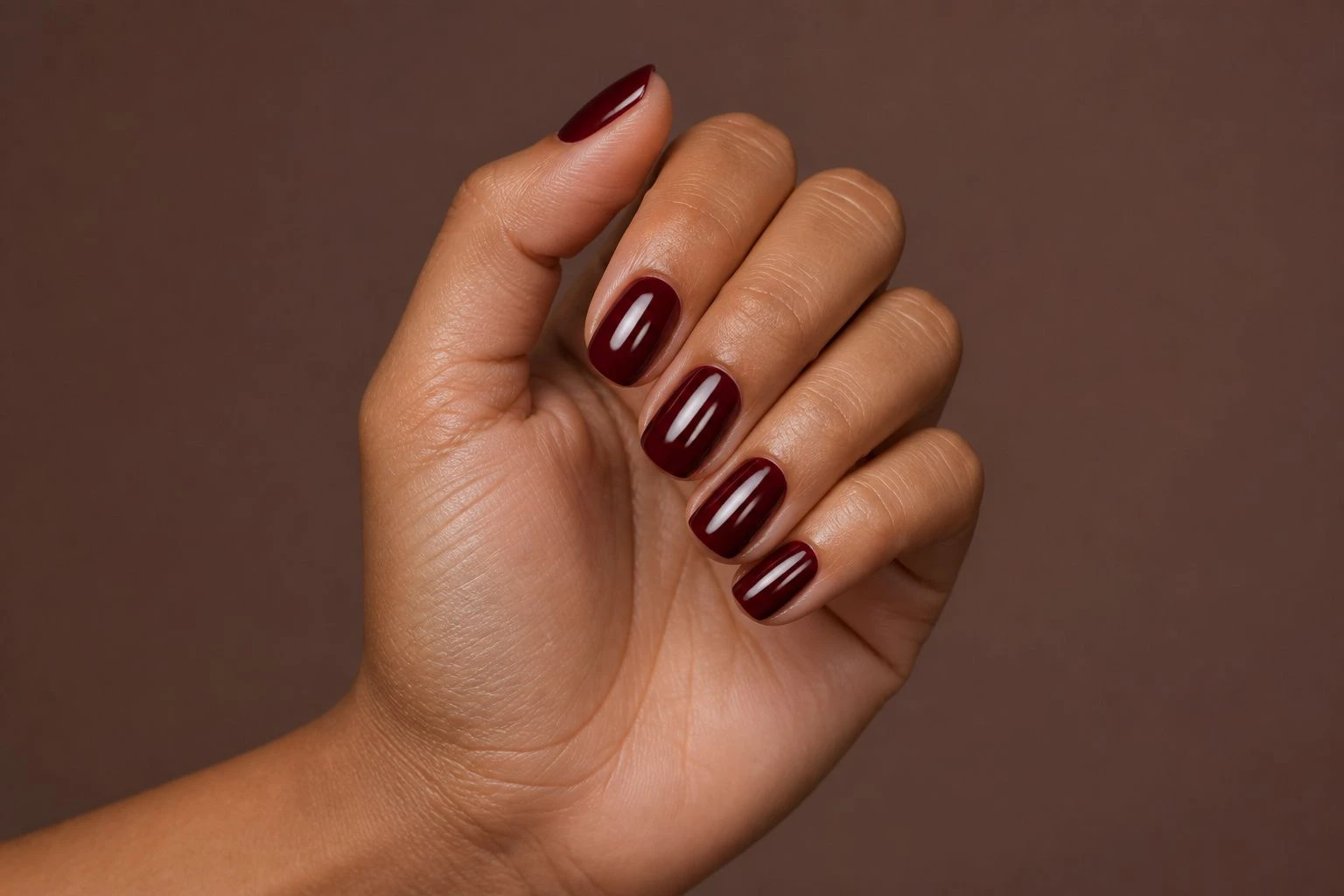 Rounded Burgundy autumn nails on a woman’s hand, rounded shape, hand-only studio macro shot.