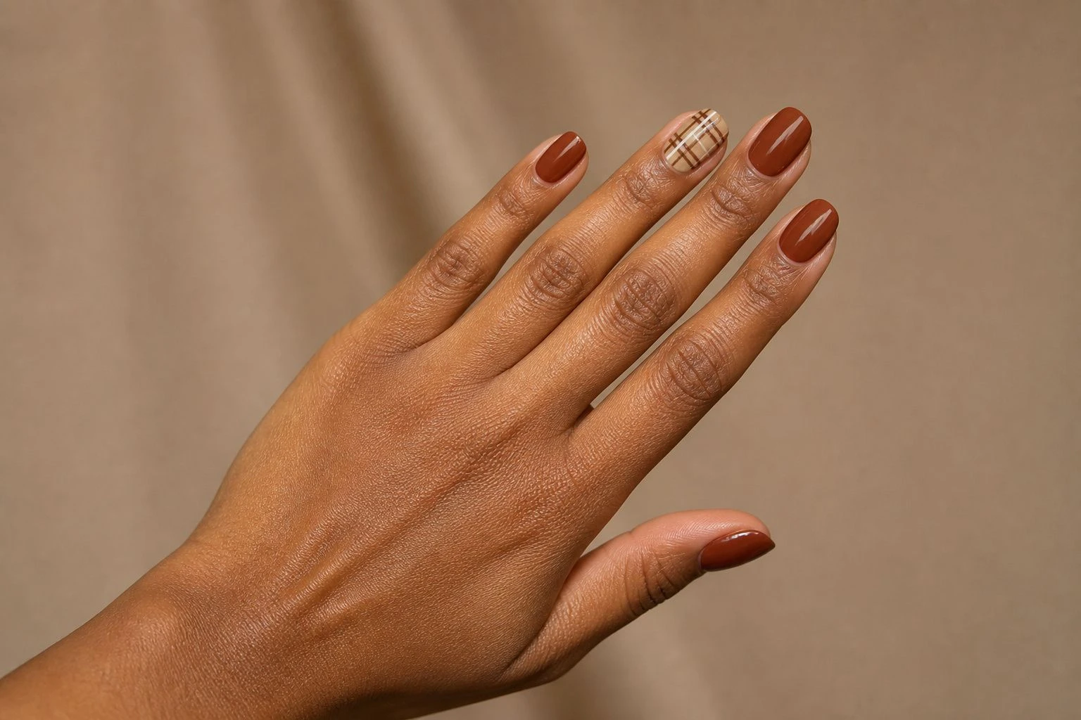 Autumn Plaid Accent nails on a woman’s hand, hand-only studio macro shot.