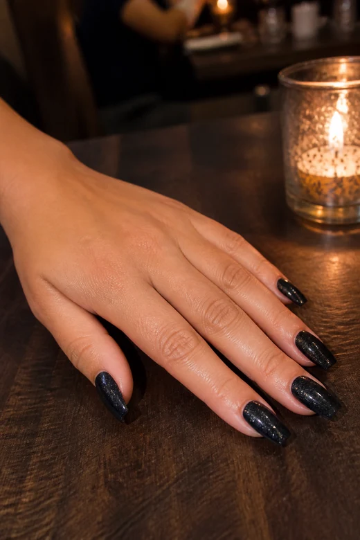 Black nails with fine charcoal glitter on a woman’s full hand