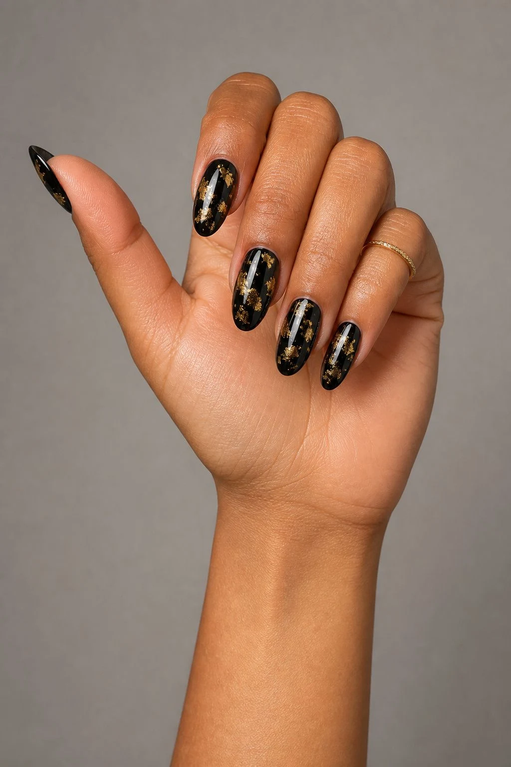 Black Christmas nails with antique gold foil in a curled hand pose with a delicate gold ring