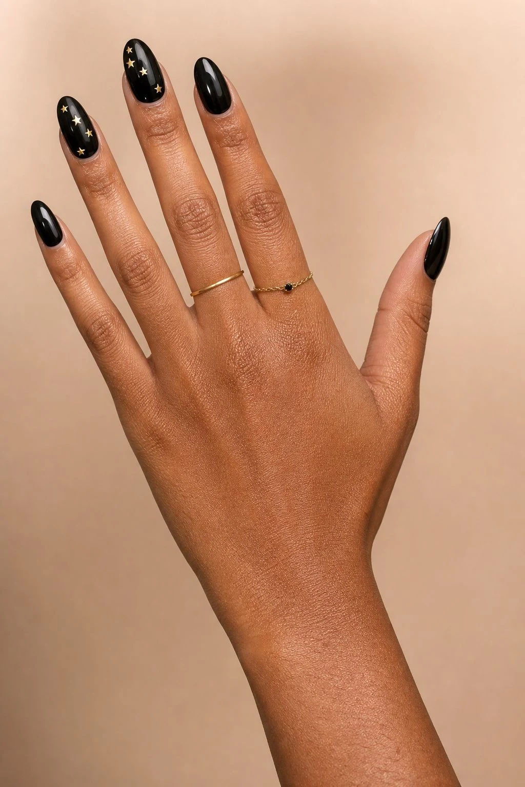 Black nails with tiny gold star accents and delicate gold rings
