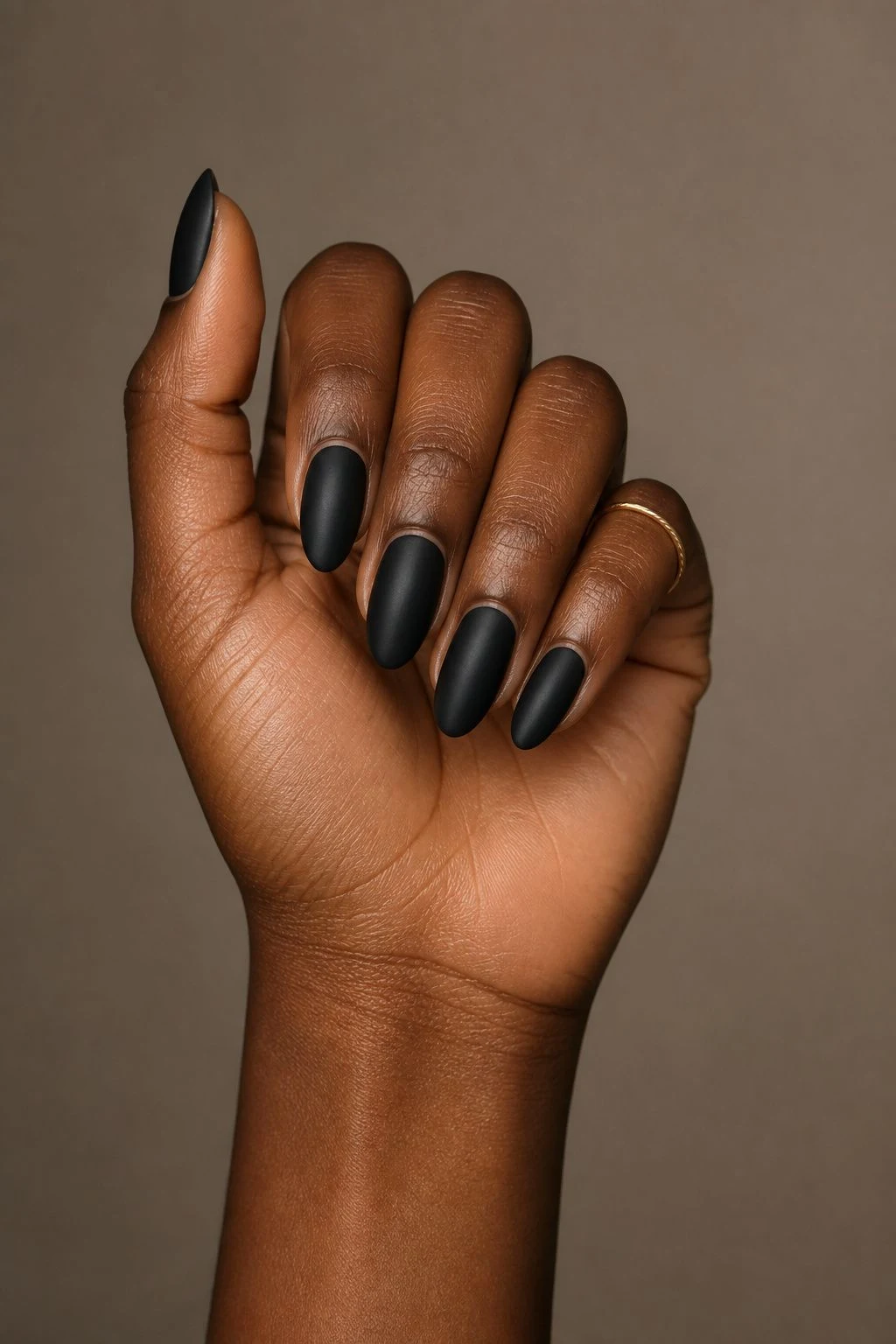 Matte Black Almond Christmas nails in a curled hand pose with a delicate gold ring