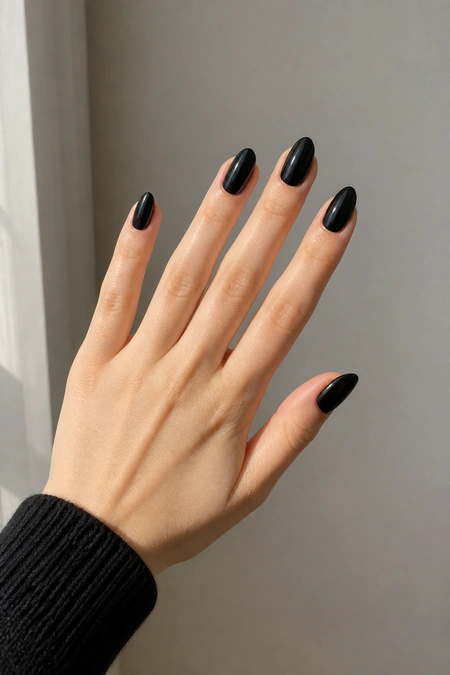 Glossy black oval nails on a fair skin tone hand in a relaxed diagonal fan pose with visible wrist and short partial forearm, natural daylight