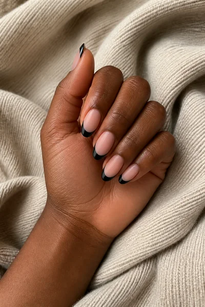 Black French tip nails with a matte base on a deep brown skin tone hand in a side angled display with visible wrist and short partial forearm, natural daylight
