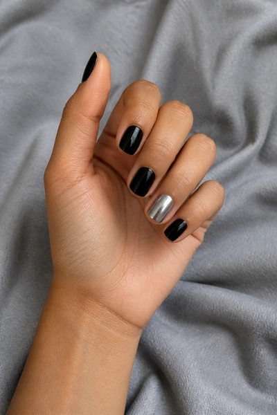 Short black nails with one silver accent on a light brown skin tone hand in a gentle pinch pose with visible wrist and short partial forearm, natural daylight
