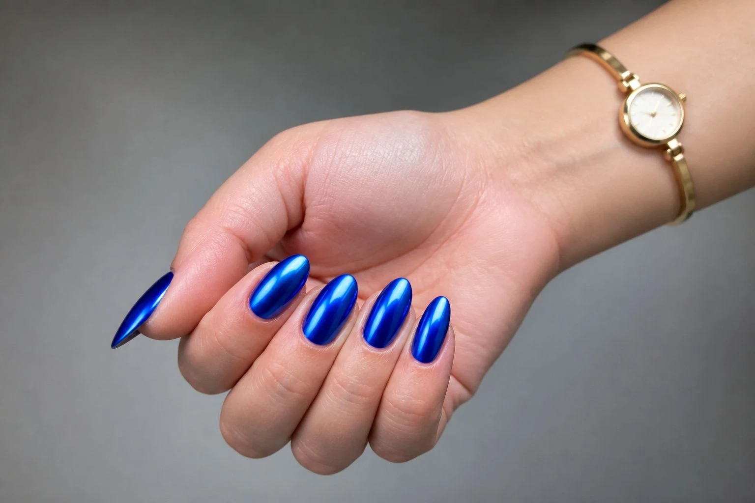 Cobalt blue chrome almond Christmas nails in a curled hand pose with a delicate gold watch