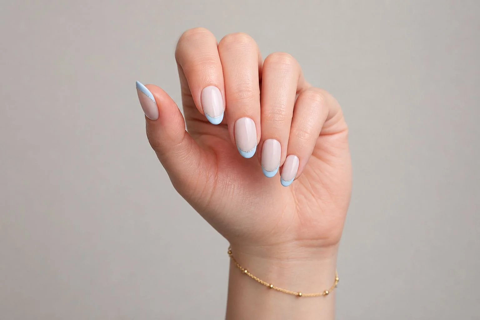 Curled hand showing a soft icy blue micro French almond manicure with a delicate silver line accent and gold bracelet