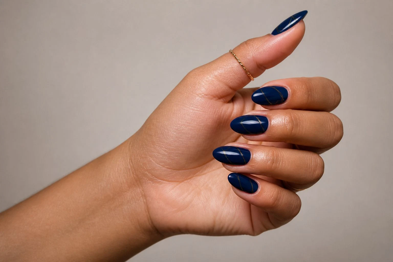 Navy blue nails with a fine gold line in a side profile pose with a delicate gold ring