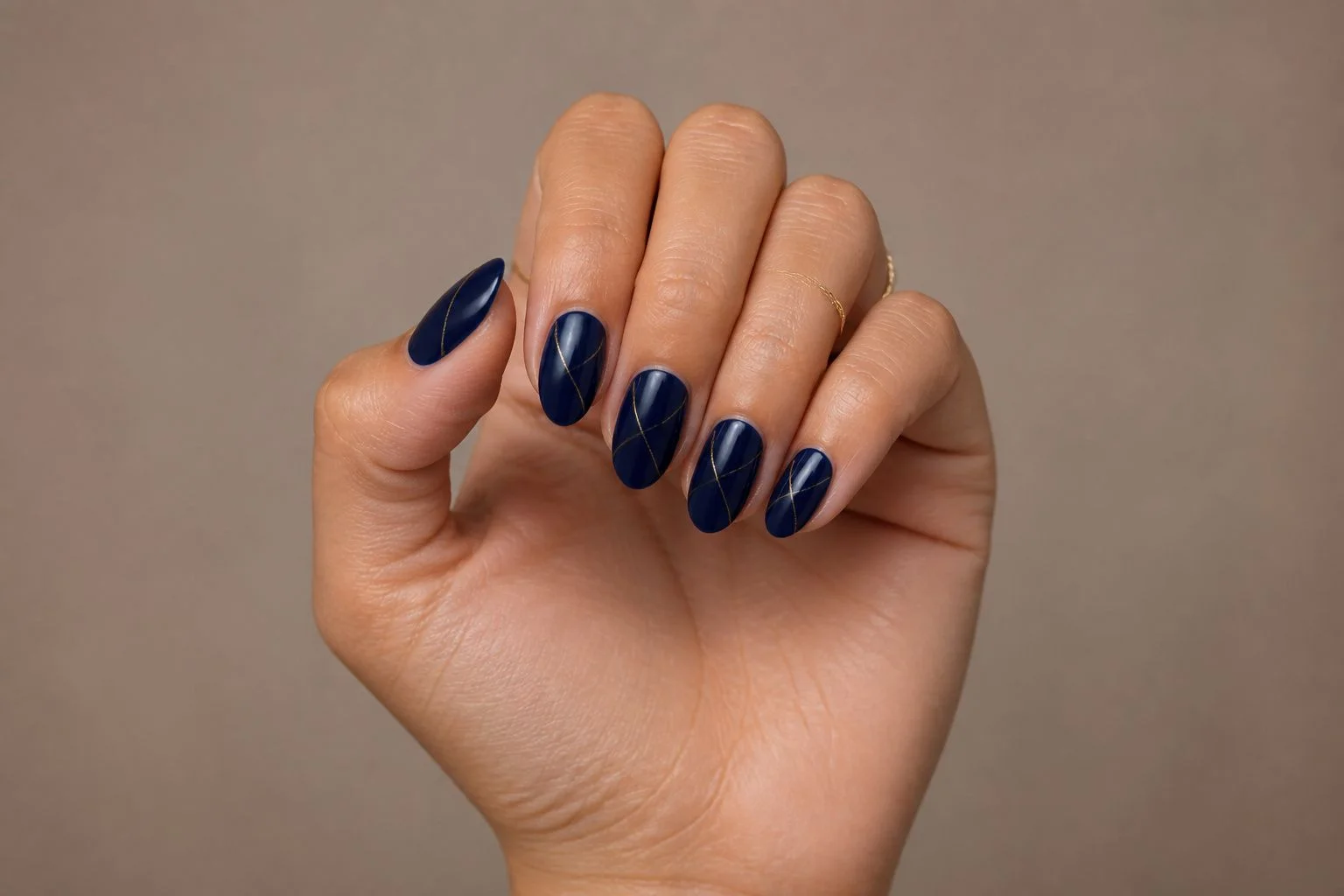 Curled hand showing a glossy navy blue almond manicure with a fine gold line accent and a delicate gold ring
