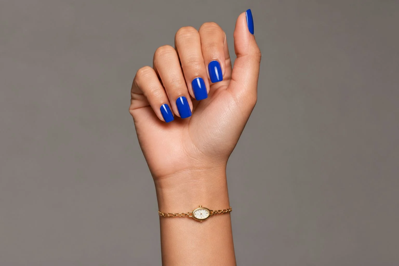 Royal cobalt blue square Christmas nails with a slim gold watch, curled finger pose