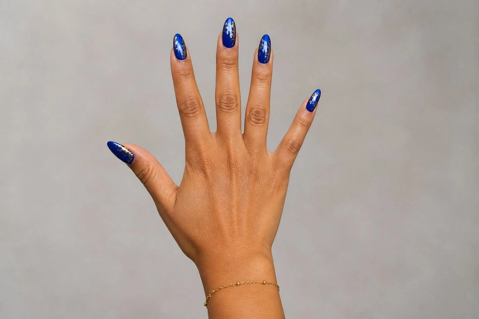 Sapphire blue nails with gold foil in an open palm pose with a delicate gold bracelet