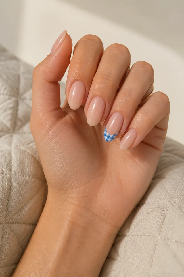 Blue gingham French accent on one almond nail with sheer base, glossy finish, medium olive skin, hand lifted in natural window light with forearm connected