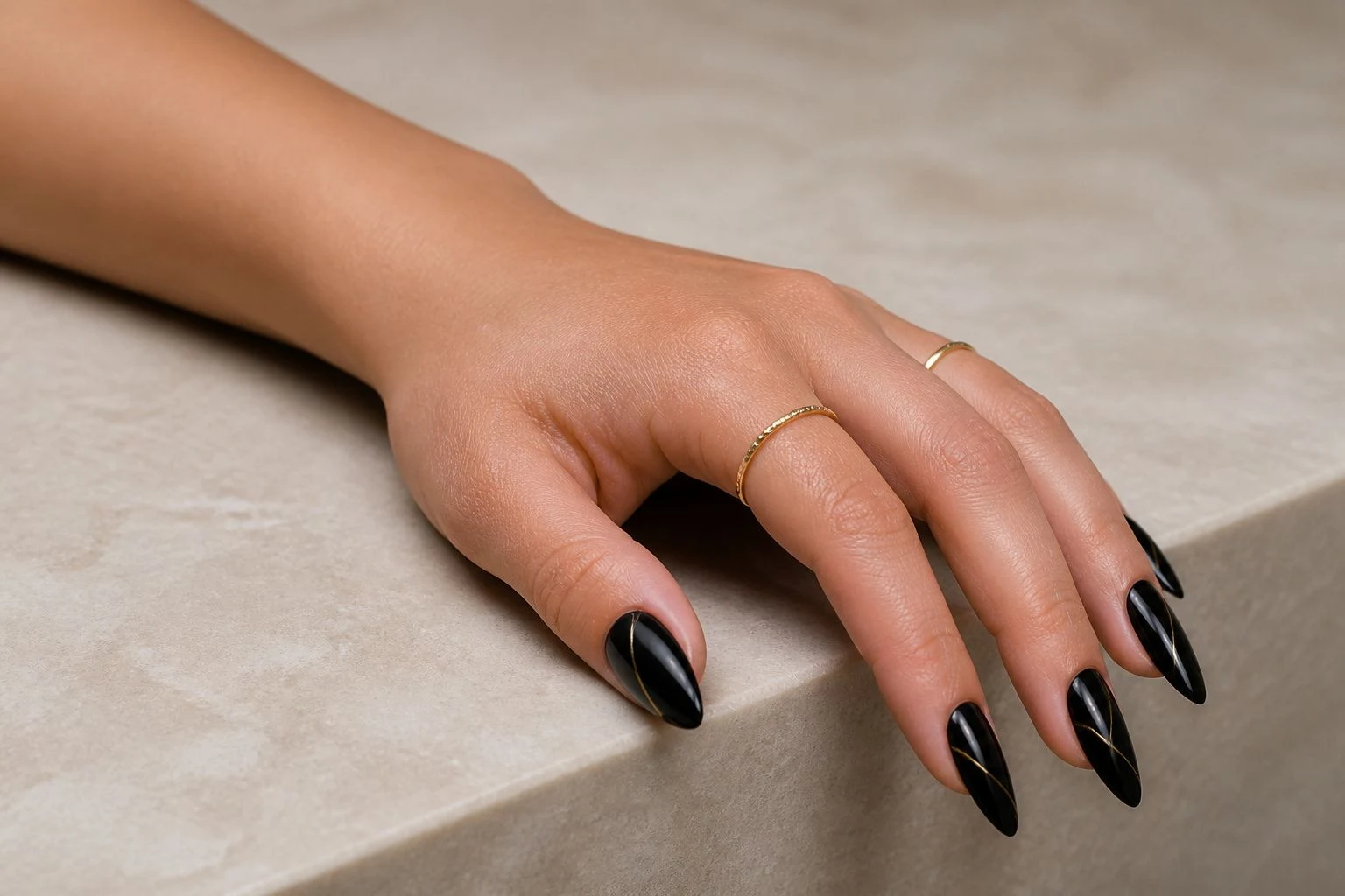 Black Christmas nails with a refined gold accent resting on a surface edge with delicate gold rings