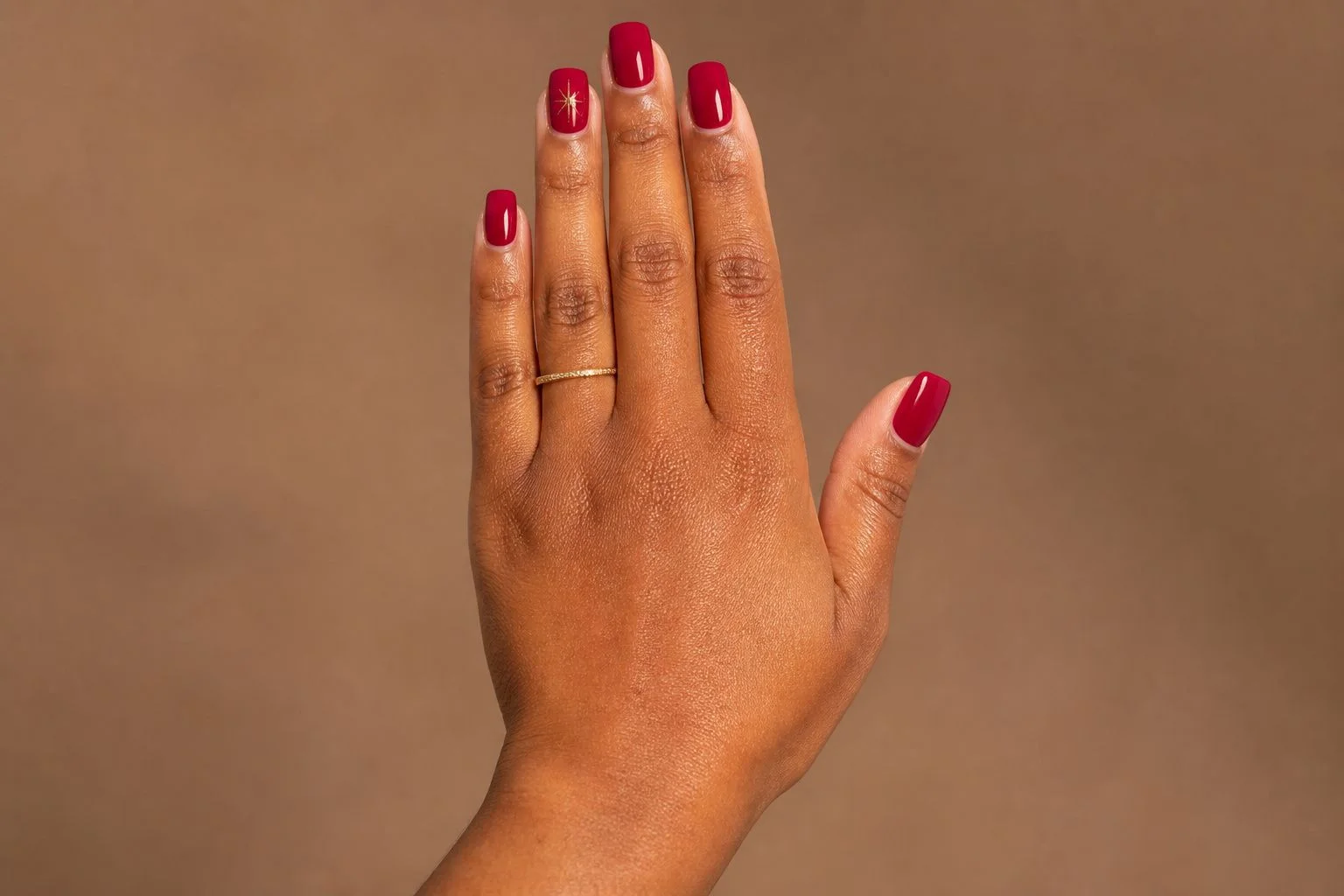 Cranberry red square Christmas nails with a delicate gold star accent nail, back of hand pose