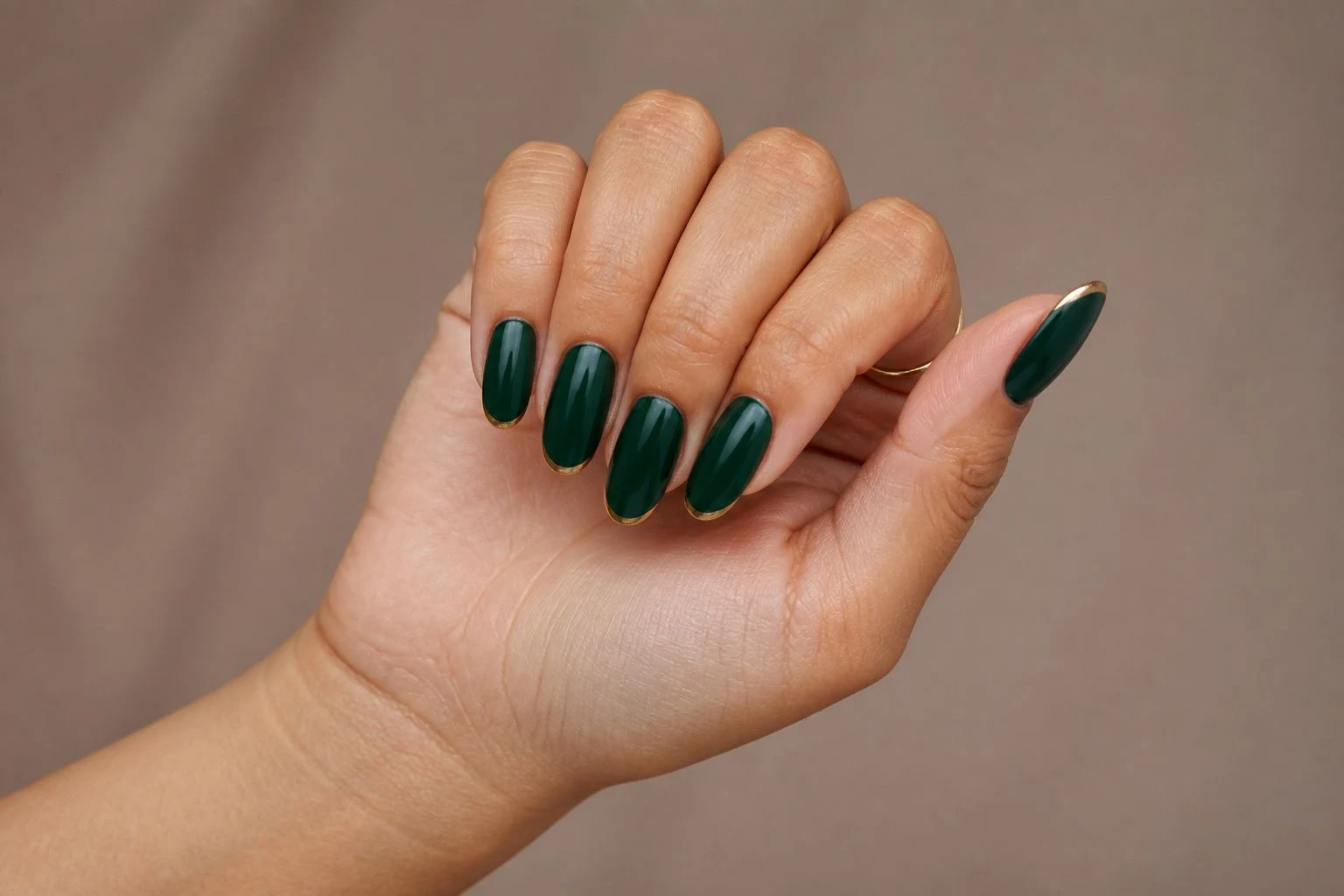 Emerald and gold almond French Christmas nails in a curled hand pose with delicate gold rings