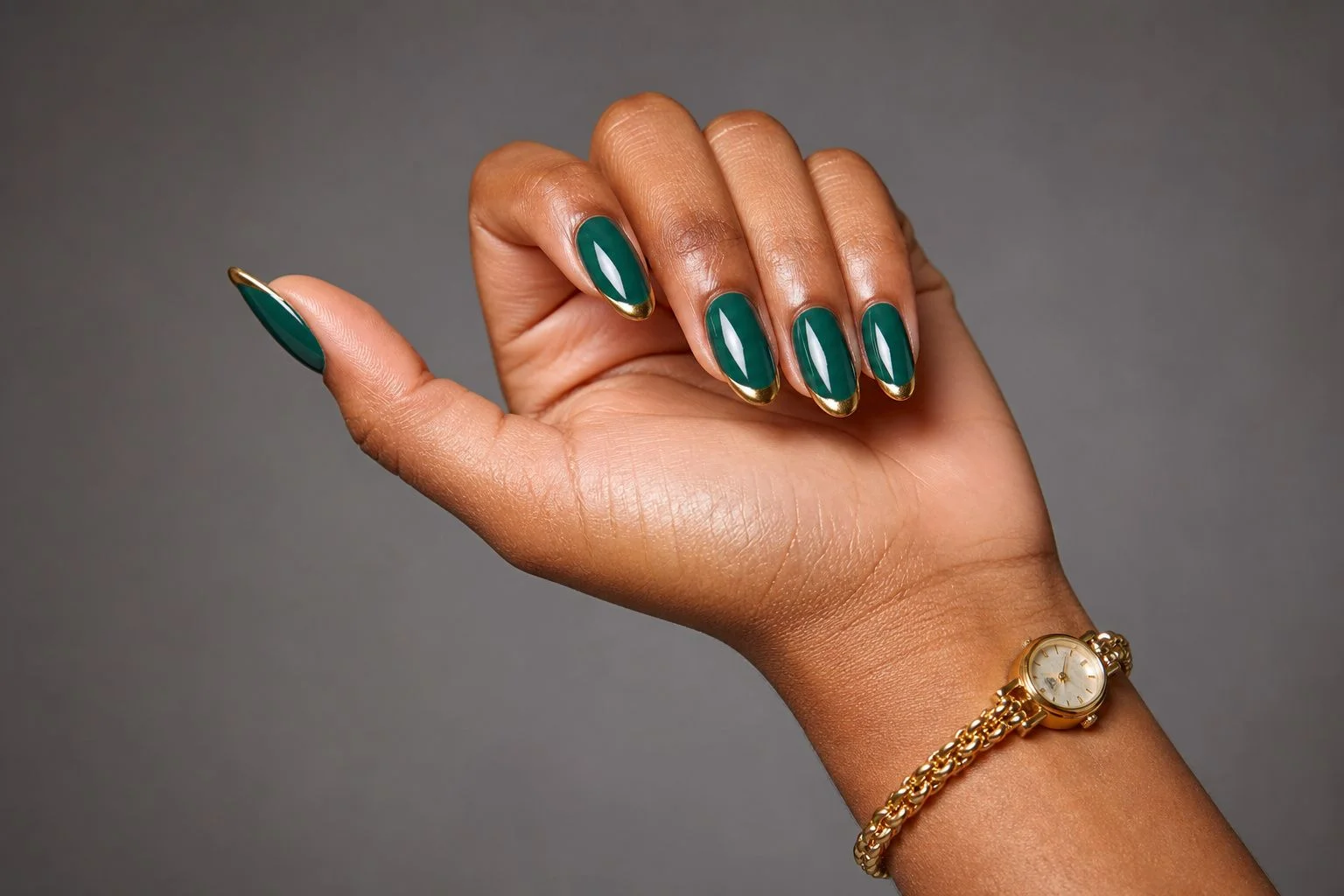 Palm up curled hand showing a glossy emerald green almond French manicure with a delicate gold tip and a slim gold watch