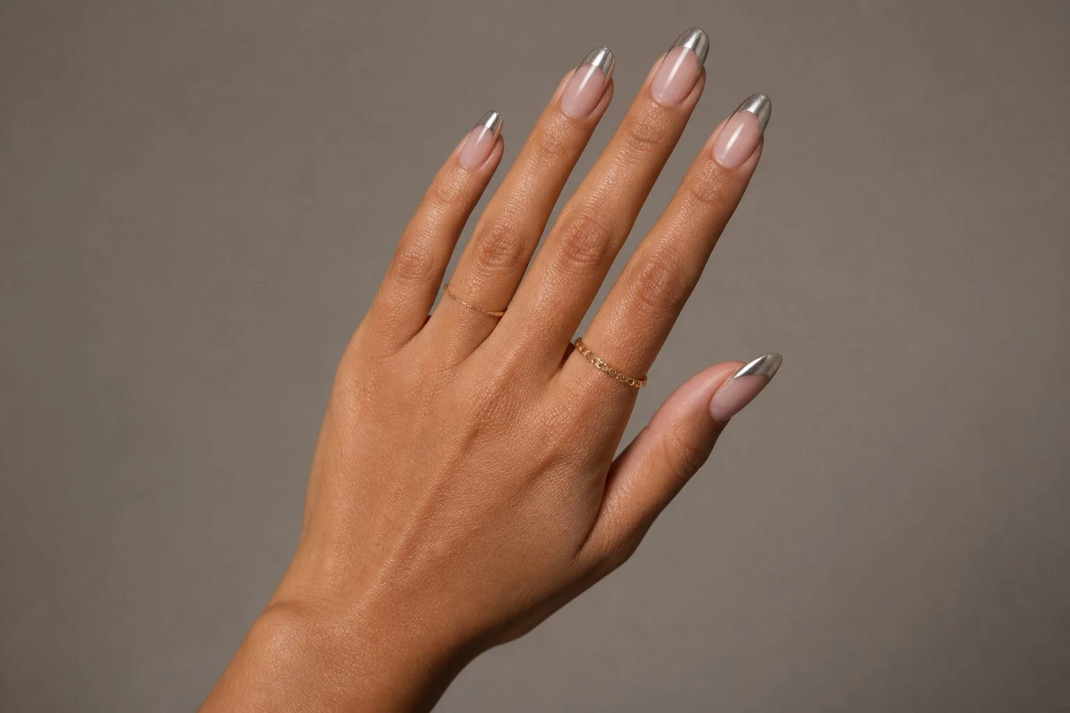 Silver chrome micro French Christmas nails in a natural fan hand pose with delicate gold rings