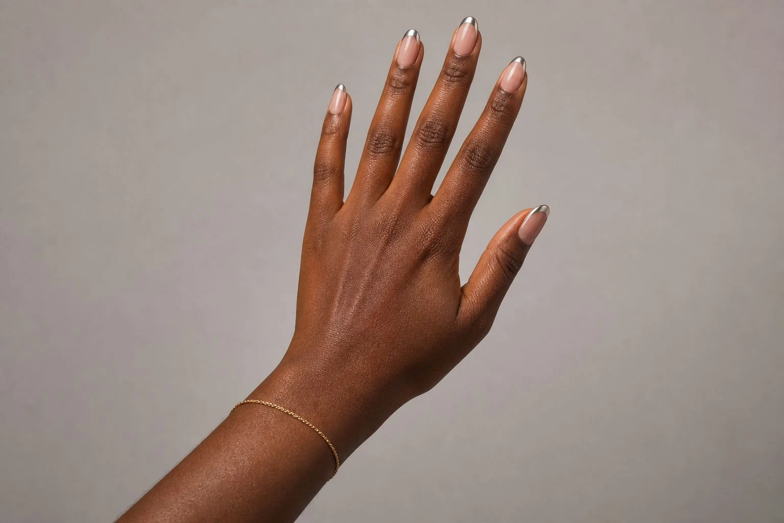 Silver chrome micro French Christmas nails with a delicate gold bracelet, reaching hand pose